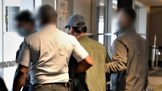 Binjun Xie is escorted to a plane after being arrested.