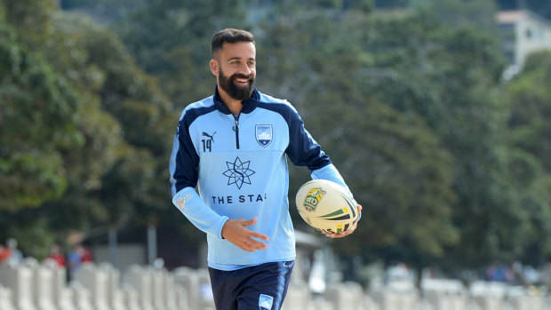 Whole new ballgame: Alex Brosque swaps the round ball for the oval variety at Sydney FC's recovery session at Balmoral Beach on Monday.