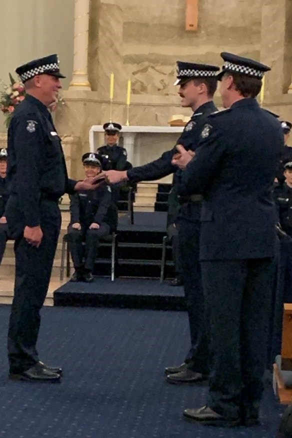 Andrew Wilson’s son Tom hands him his police badge while Chief Commissioner Shane Patton watches on.