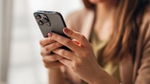 Woman smiling while holding and interacting with a smartphone, representing modern communication, digital connectivity, and mobile technology in a professional or casual setting