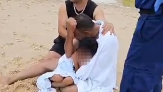 The boy’s visibly upset father clutches onto one of his other children after unsuccessful attempts to rescue his eldest son.