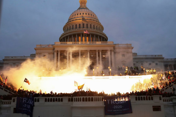 A flash lights up the front of the US Capitol as a mob of Trump supporters control the steps of the building.