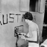 Greg Shackleton painting the word ’Australia” and a flag on the wall of a building in Balibo.