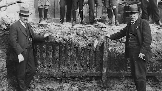 Men pose in front of the picket fence unearthed in the early 1920s during excavation work for the Capitol Theatre on Swanston Street.