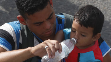 A man carrying a boy gives the child water while walking with a caravan of Central American migrants heading for the US.