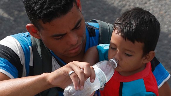 A man carrying a boy gives the child water while walking with a caravan of Central American migrants heading for the US.