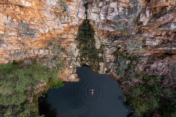 Aerial photo of a woman relaxing in a natural rock pool surrounded by red cliffs