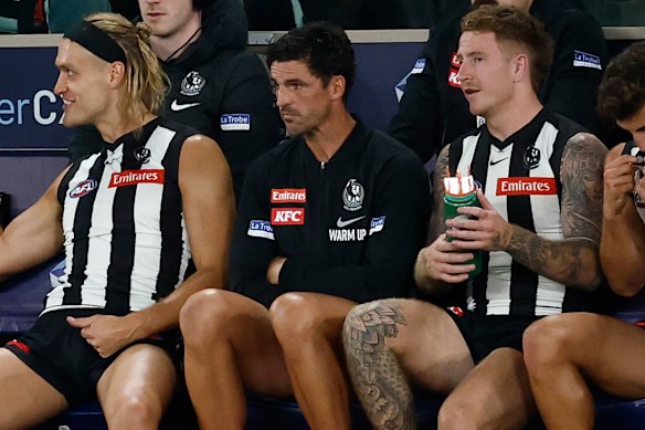 Darcy Moore (left) and Scott Pendlebury (centre) watch on from the bench.