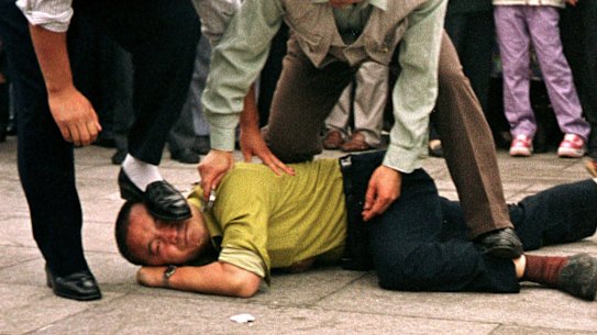 Police detain a Falun Gong protester in Tiananmen Square as a crowd watches in Beijing.