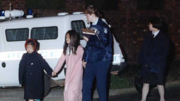 The younger sisters of Karmein Chan, 13, are led away from their Templestowe home by a policewoman.