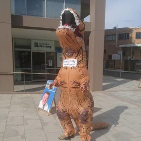 Peter Thompson wearing the dinosaur suit which bears the name 'Craig Kelly Denialosaur'. 