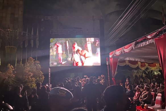 Onlookers watch vision of the Bali bombing aftermath on a big screen at the 20th anniversary memorial of the event in Kuta, Bali.