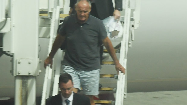 Chris Dawson is escorted by NSW Police detectives off a Qantas flight as he is extradited from the Gold Coast.