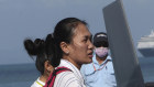 Cambodian medical officers unload equipment from a helicopter as they prepare for health checks on passengers and crew of the Westerdam, seen in the background.