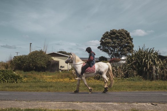 A youth rides a horse through the quiet streets of Marokopa.