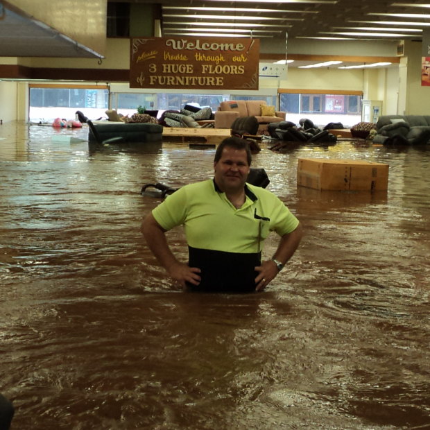 Rowes warehouse manager Wayne Miller stands waist deep in floodwater as furniture floats out to Russell Street.
