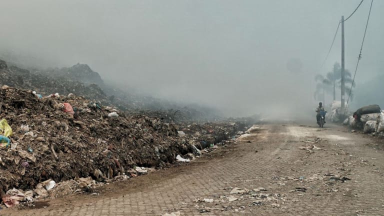 A scooter drove through the thick smoke from the Suwung dump site fire.