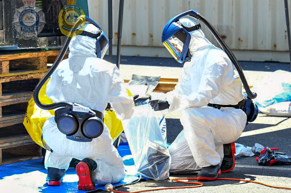 Forensic officers in bio-hazard suits removing the illicit substances from the shipment.