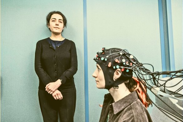 Researcher Mehrnaz Shoushtarian (left) and a colleague demonstrate a cap fitted with light sensors used to show brain activity in people with tinnitus.