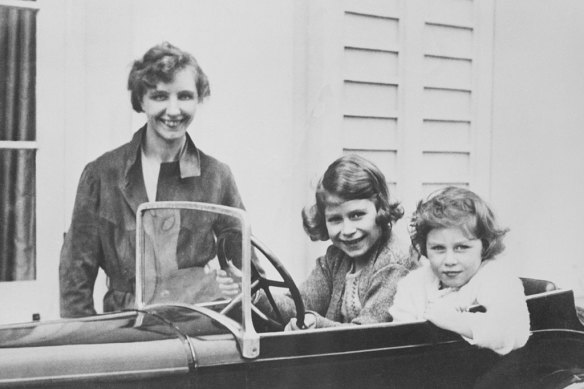 Princess Elizabeth and her younger sister Princess Margaret play in a miniature automobile while their governess, Marion Crawford, keeps an eye on them.