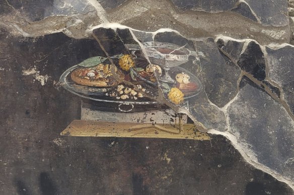 The wall of an ancient Pompeian house with a fresco depicting a table with food. 