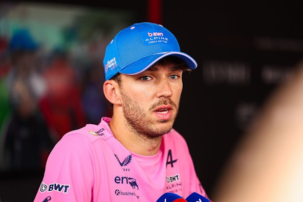 A man in a pink Alpine F1 shirt speaks to media. 