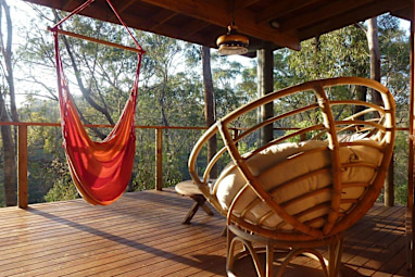 A sunlit balcony with a comfy chair and hammock overlooking bushland