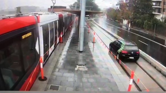 A motorist drives along a section of a track beside a light rail stop. 