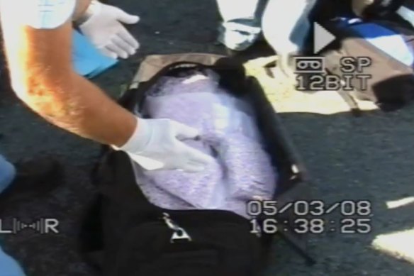 Officers search the black sports bag containing nearly $8 million worth of drugs stored in the cargo hold. 