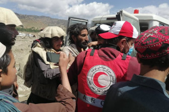 Afghans gather around first responders as they provide aid to villagers from the back of a four-wheel drive.