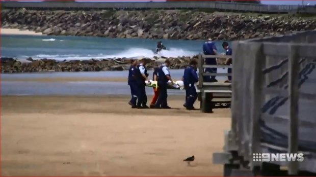 Police remove the body of a man who died after trying to save his son at Urunga Beach.