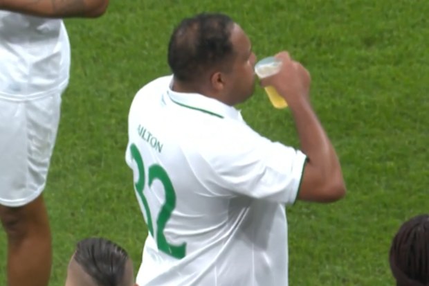 Ailton is seen taking a sip of a pint on the sidelines.