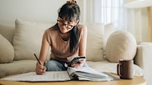 A woman sits at her living room with smartphone and financial reports doing her monthly budget.