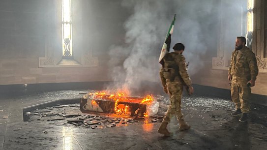 Rebel fighters stand next to the burning grave site of Syria’s late president Hafez al-Assad at his mausoleum in the family’s ancestral village of Qardaha in the western Latakia province.