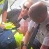 A still from footage of the boy being restrained by a Jetstar worker, passenger Barry Clark and the pilot.