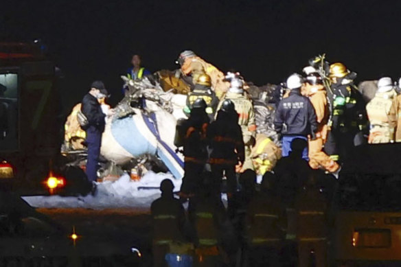 Firefighters inspect a part of the Japanese coast guard aircraft on the runway of Haneda Airport on Tuesday.