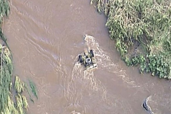 An emergency rescue team works to remove a ute from fast-moving floodwater in Canungra, amid the search for a missing man.