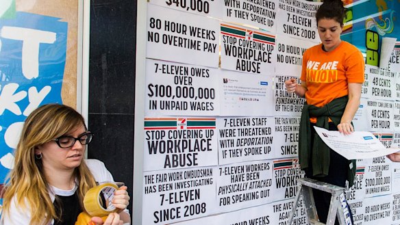 Protesters from the Young Workers' Centre pin signs to the windows of Melbourne 7-Eleven store highlighting the company's worker exploitation and wage fraud scandal.  