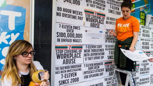 Protesters from the Young Workers' Centre pin signs to the windows of Melbourne 7-Eleven store highlighting the company's worker exploitation and wage fraud scandal.  