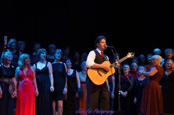 ABC broadcaster Nick Rheinberger singing here with Tina Broad (right) and Shoalhaven Mayor Amanda Finley (far right) part of the Glorious MUDsingers choir, who will appear in his rock opera, Watch and Act.