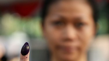 A voter poses for a photograph while showing a finger stained with electoral ink after casting her ballot at a polling station during the presidential election in Jakarta, Indonesia in 2014.
