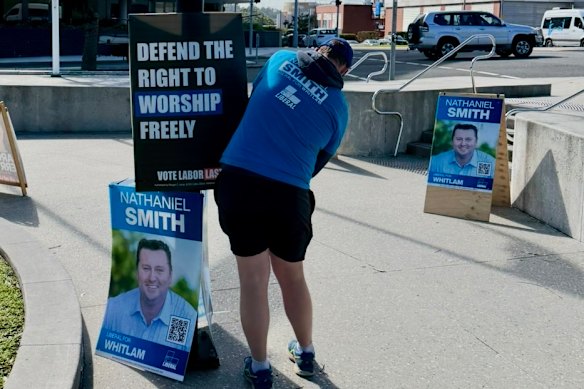 A Brethren member in shorts and a Liberal Party T-shirt puts up a poster.