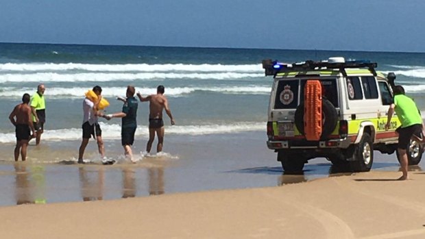 The two men are helped from the water on Fraser Island to an awaiting paramedic.