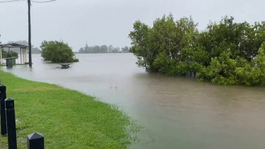 Park benches are completely under and car parks are quickly disappearing in Tumbulgum as the Tweed River overflows.