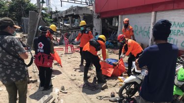 Volunteers retrieve a female body from the ruins of a shop in Talise, Palu, on Tuesday.