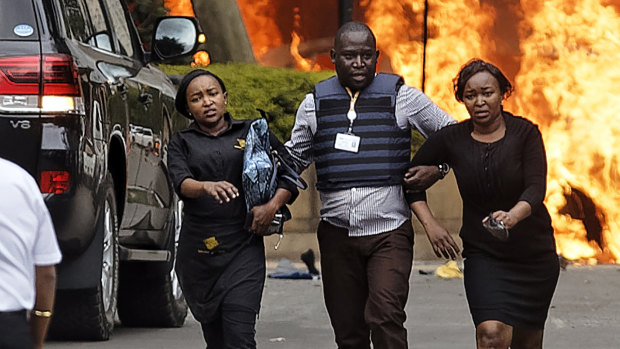 Security forces help civilians flee the scene as cars burn after an upscale hotel was attacked in Nairobi.