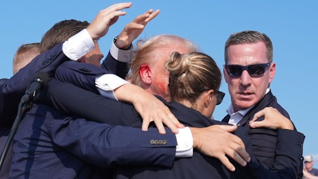 Former president Donald Trump is seen with a bloody ear as he is assisted off the stage during a campaign rally.