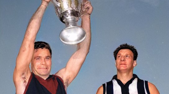 Melbourne captain Ron Barassi holds up the 1964 VFL premiership cup as Collingwood captain Ray Gabelich looks on.