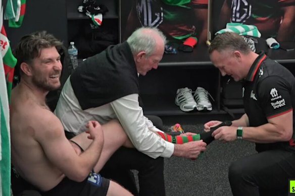 Wayne Bennett and Jason Clark help Jai Arrow get his socks on in the Rabbitohs sheds.