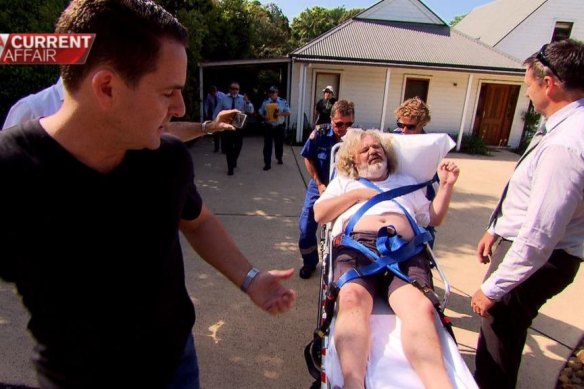 A Current Affair reporter Justin Armsden, left, watches Peter Foster on a stretcher after the discovery of Foster hiding out near Byron Bay.